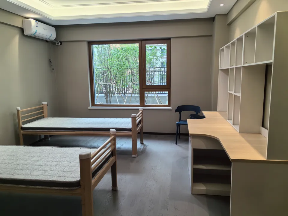 Shared dorm room with two beds, desks, shelving, and a window